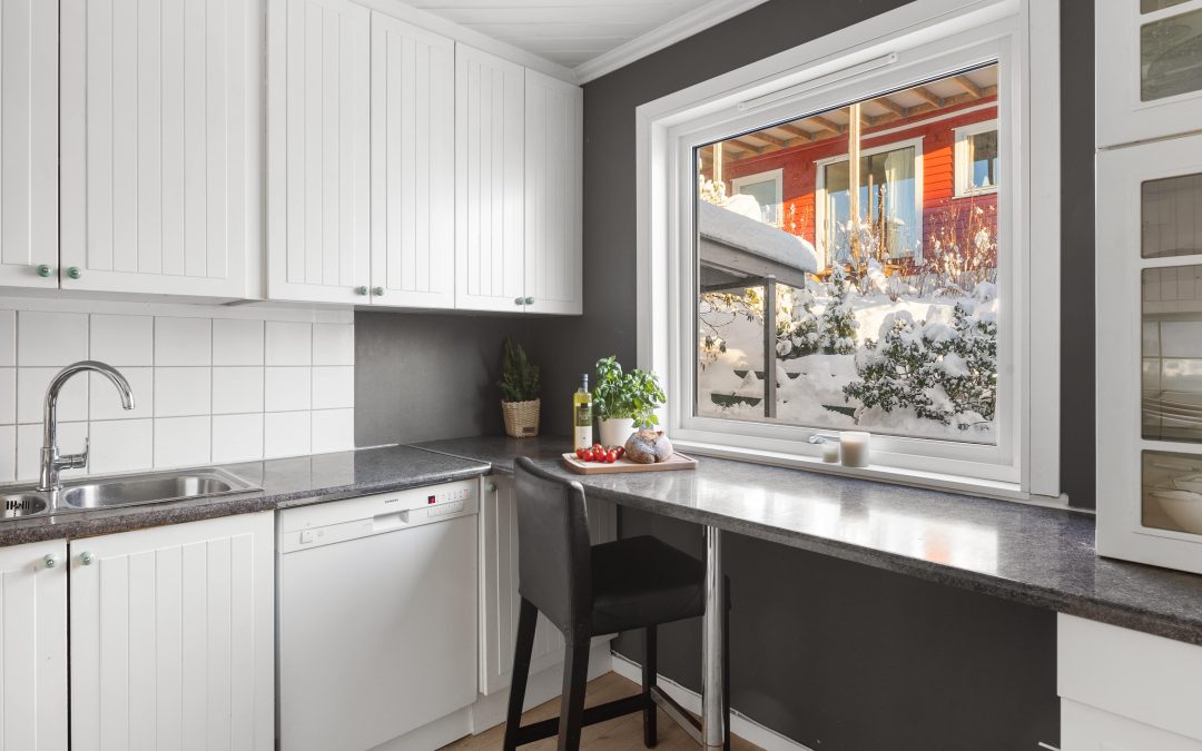 Modern de-cluttered kitchen with white cabinetry, a sink, a dishwasher, and a large window showcasing a snowy outdoor view.