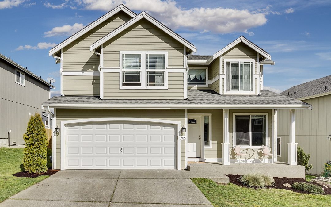 "Exterior view of a two-story house with a well-maintained front yard, a white garage door, and a porch with seating chairs.